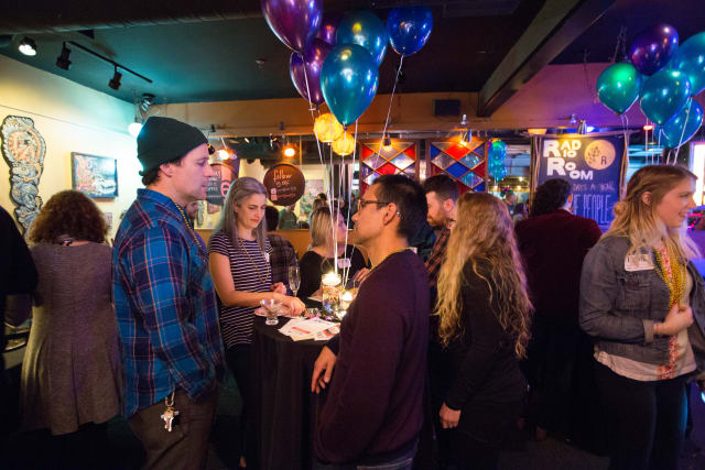 People engaging in conversation at the Love Bomb 2017 event, with colorful balloons and a festive atmosphere, highlighting community support for My Voice Music.